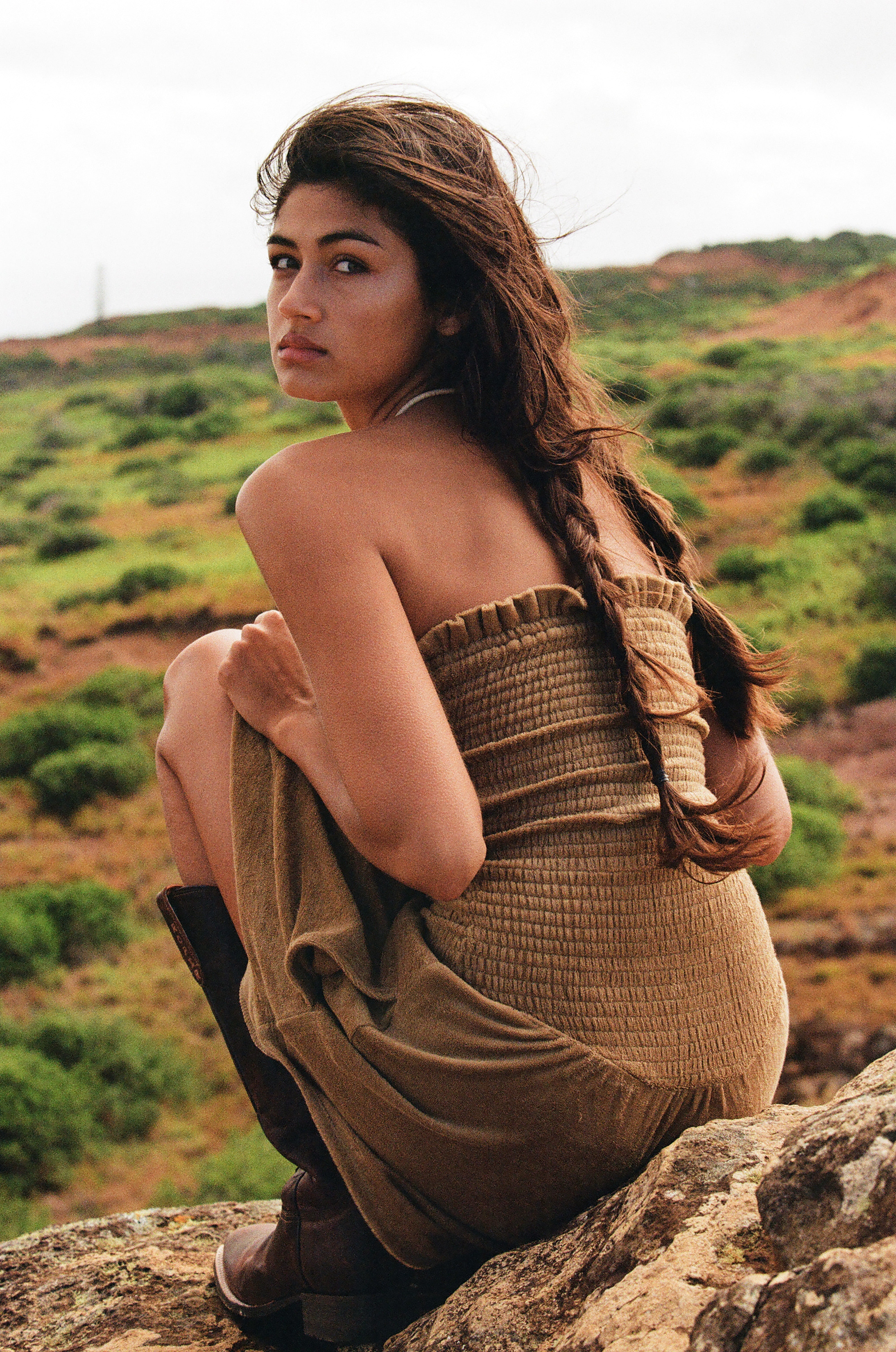 girl in beige dress and cow girl boots with braids sitting on a rock