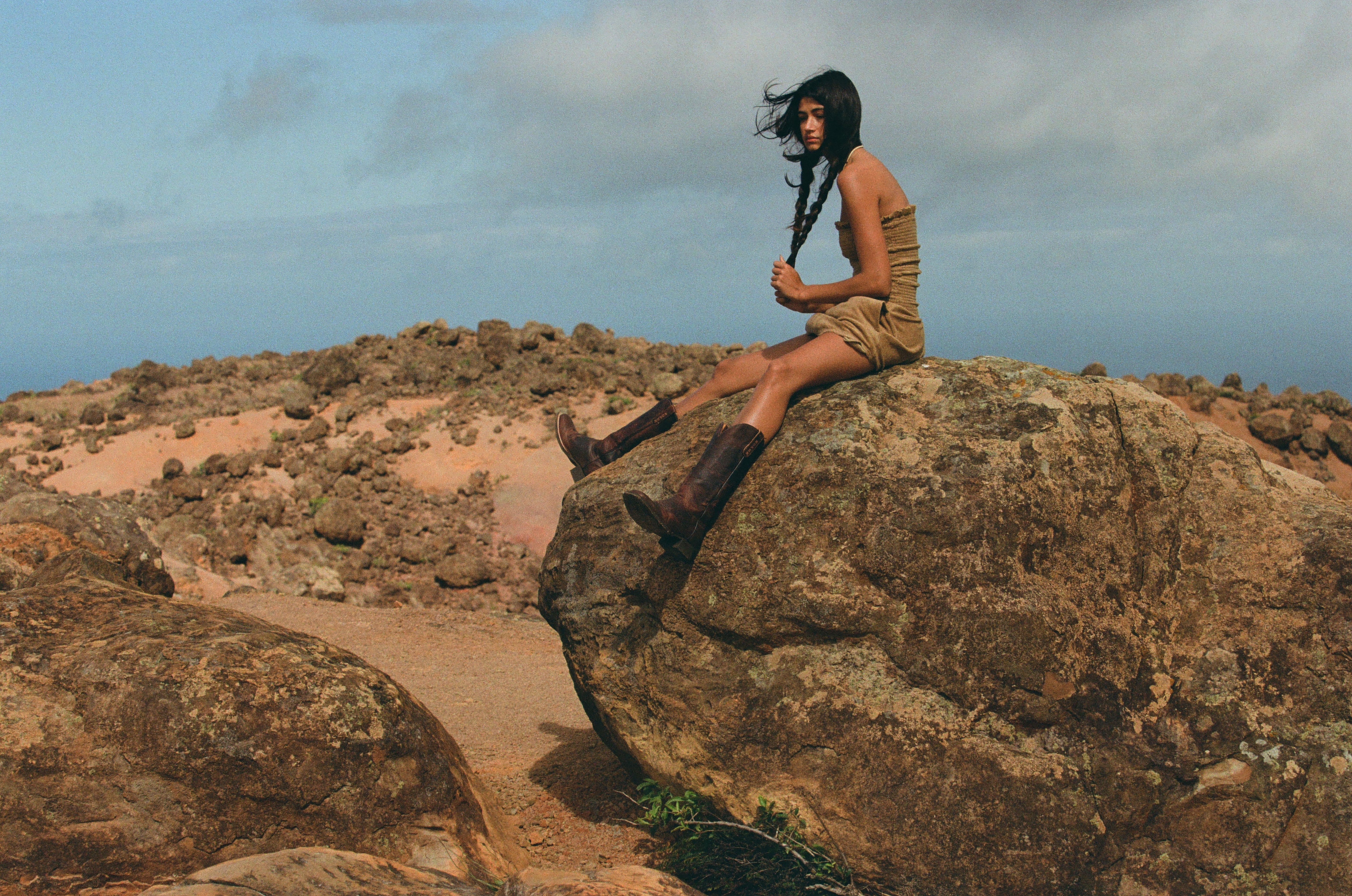 girl sitting on a rock in a beige dress with cow girl boots and braids