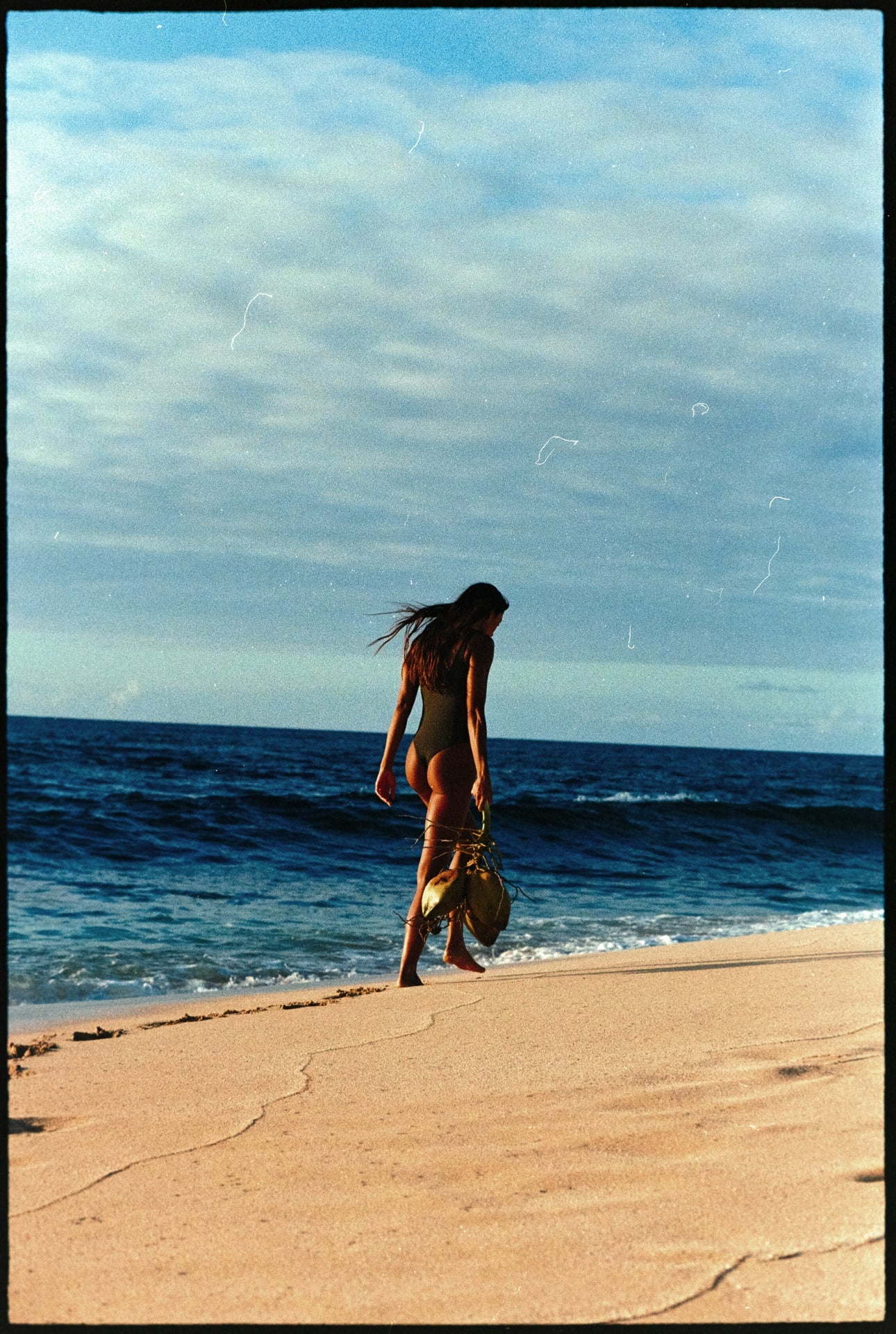 girl walking on shoreline with coconuts