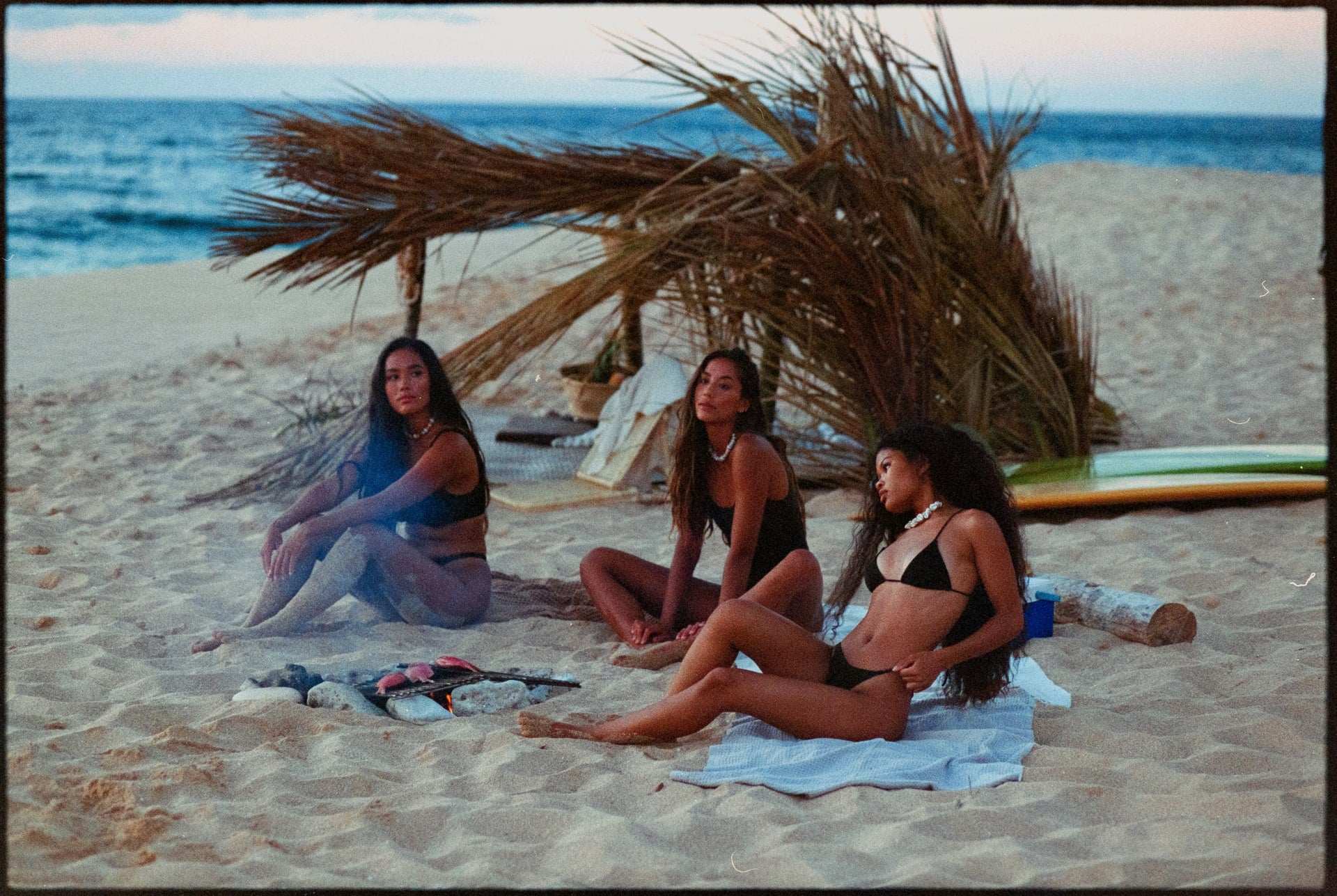 girls sitting on beach with shade shack and boards