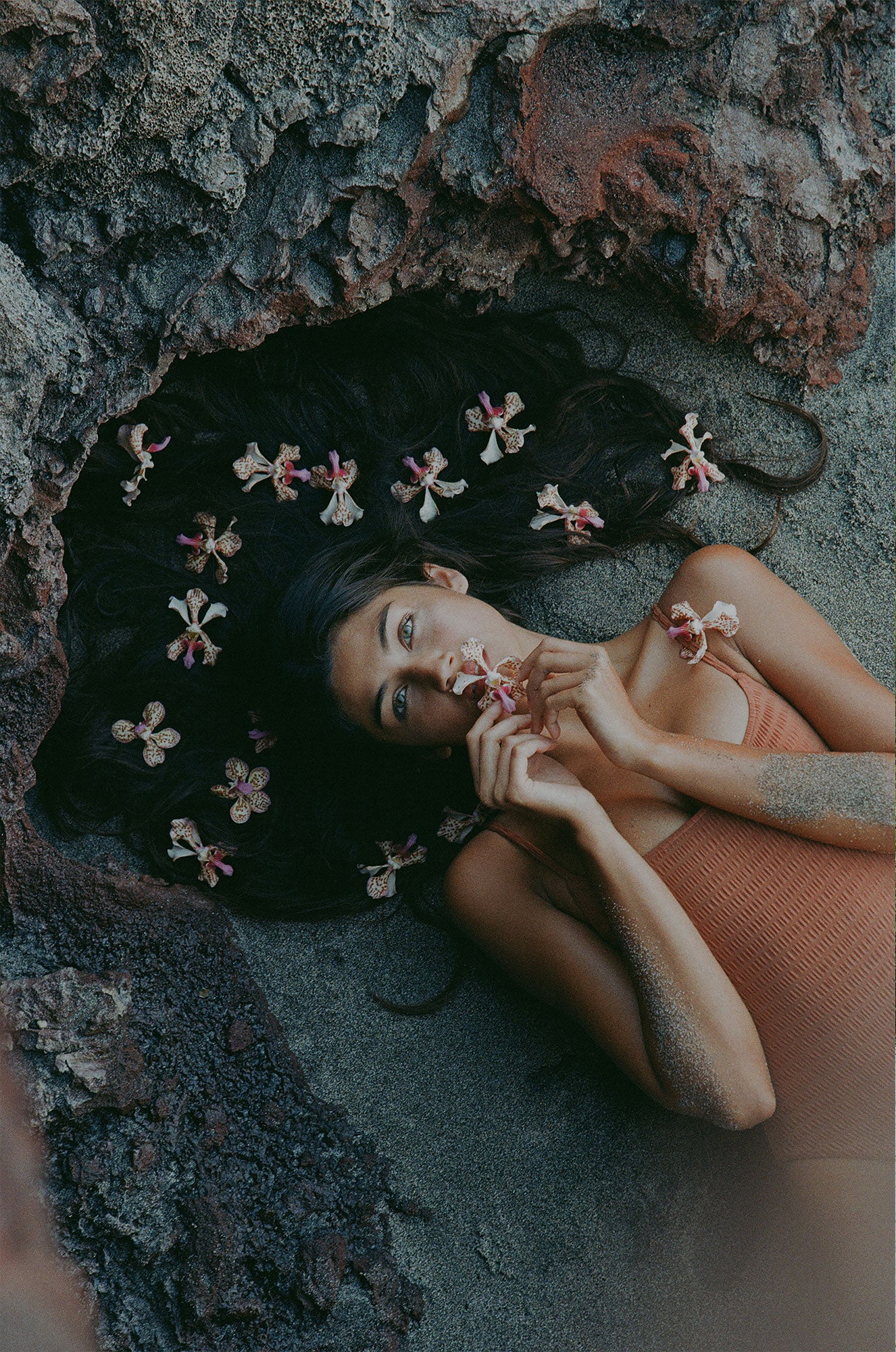 Girl lying on lava rocks with tropical flowers on her hair