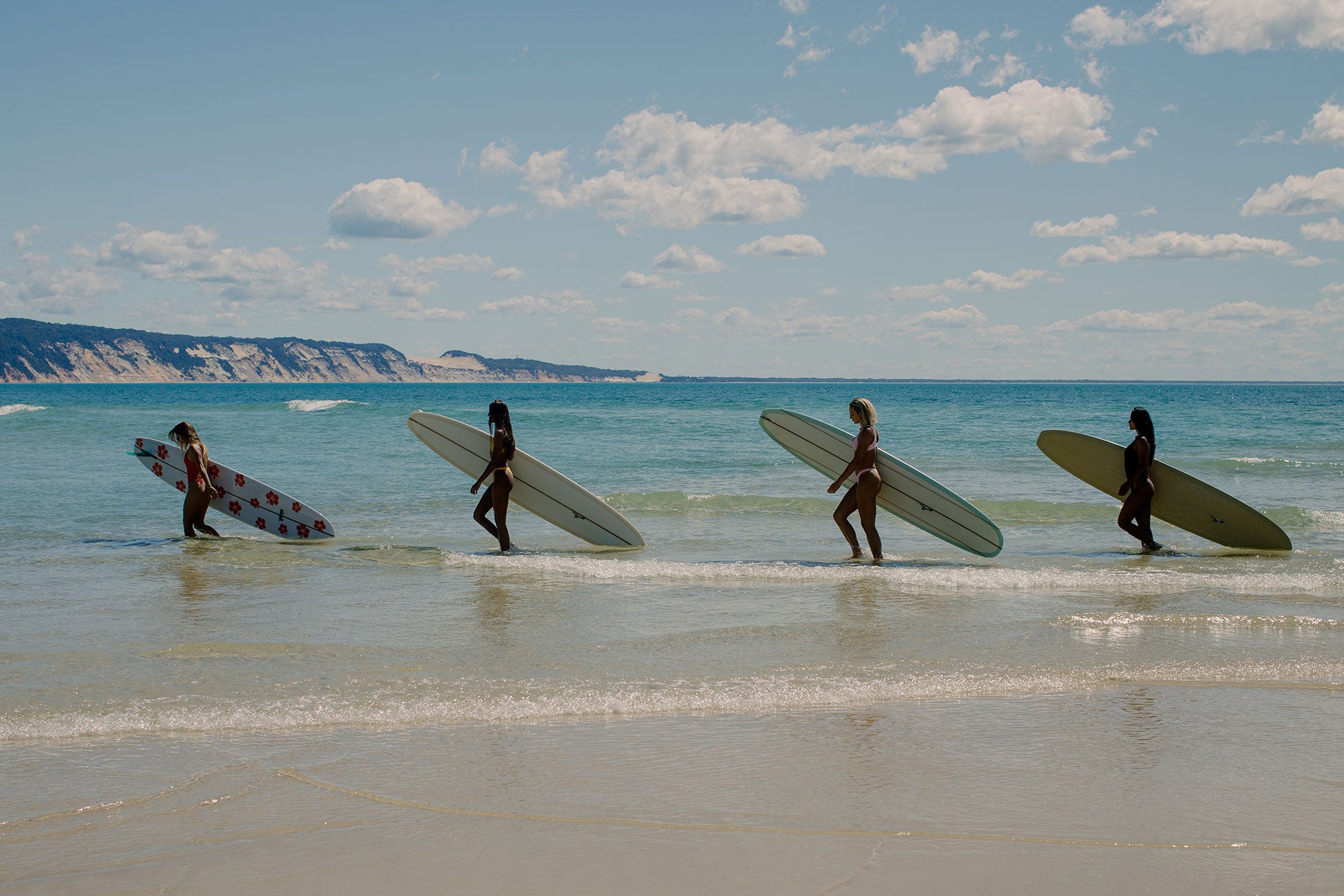 Four girls carrying longboards on the beach